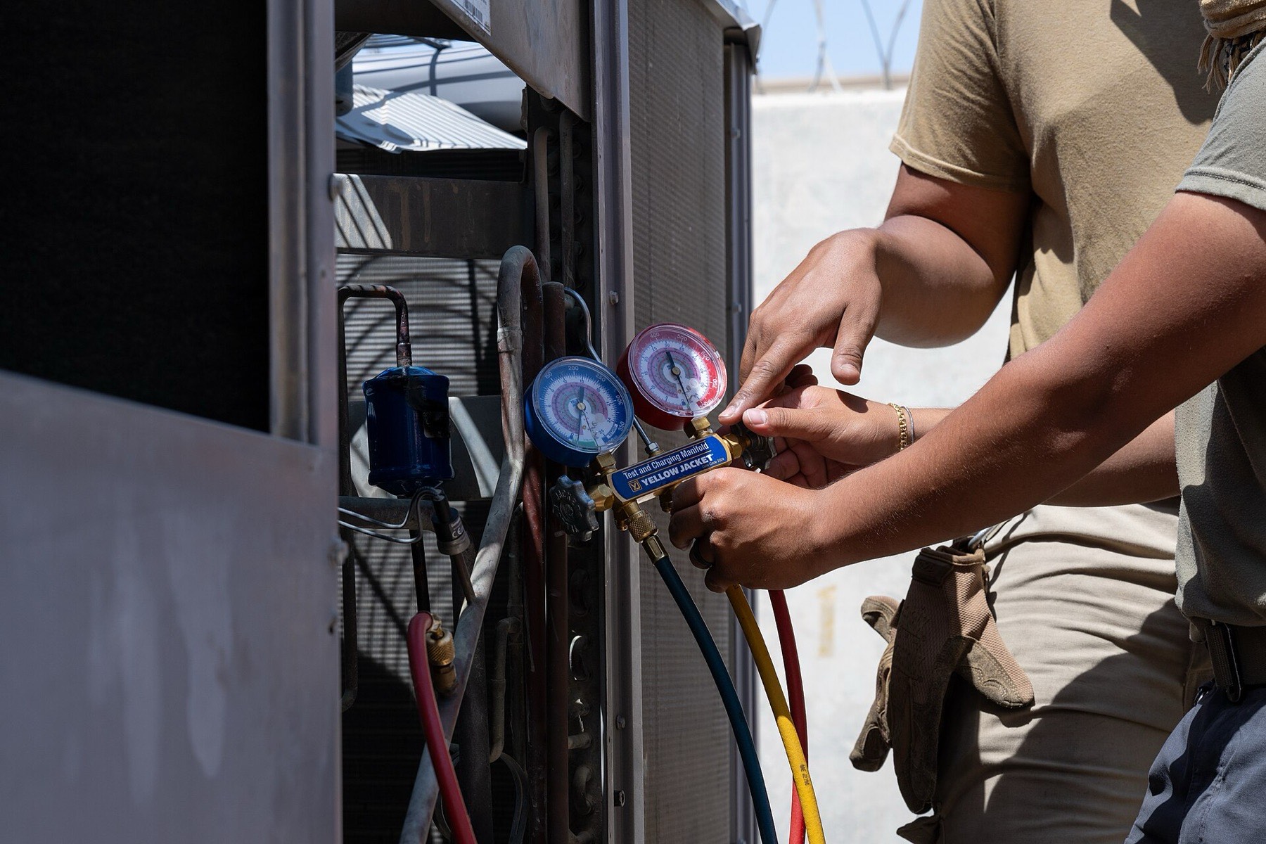 Hands connecting refrigerant gauges to an outdoor cooling unit
