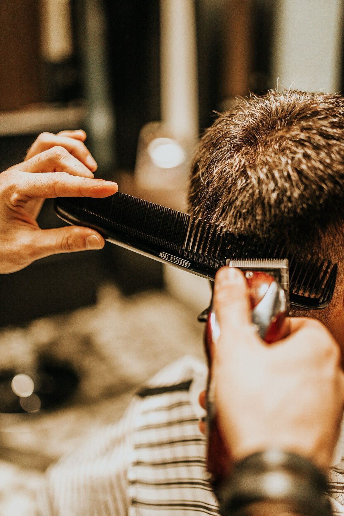 A barber shaping a fade with clippers and a comb