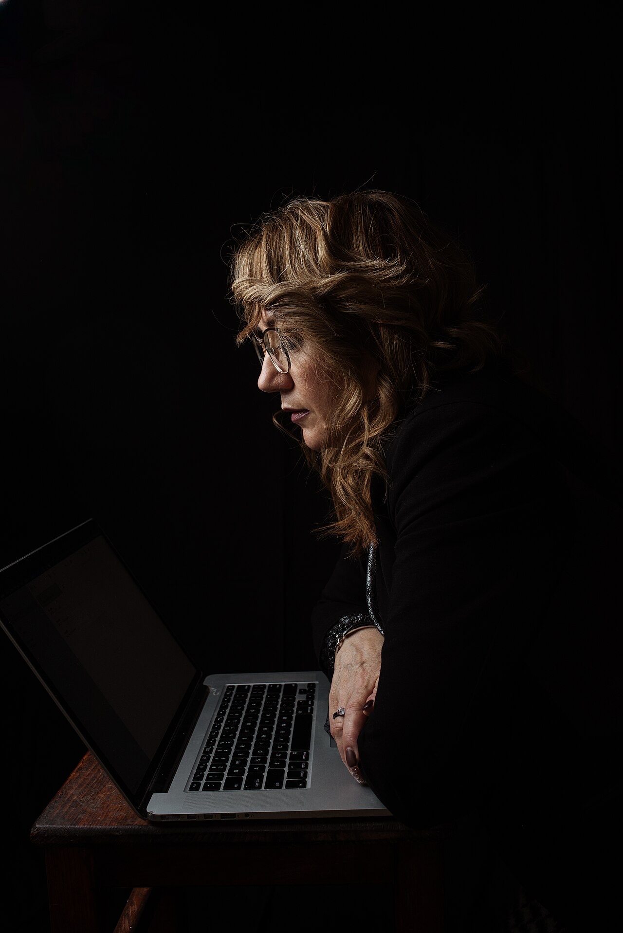 A woman leaning towards her laptop at a desk in a dark room